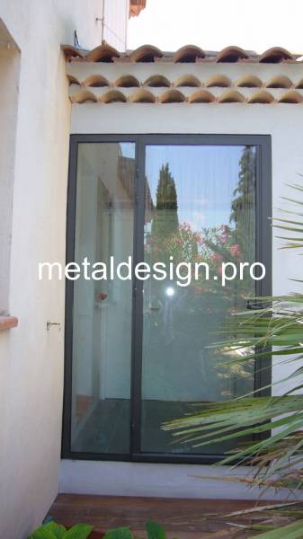 Accès par porte en verre et acier par le jardin à Célony